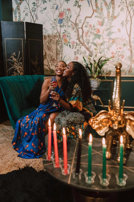 two women sitting on a couch with candles in front of them, by Julia Pishtar, trending on pexels, black arts movement, drinking champagne, loving embrace, on the altar, both laughing