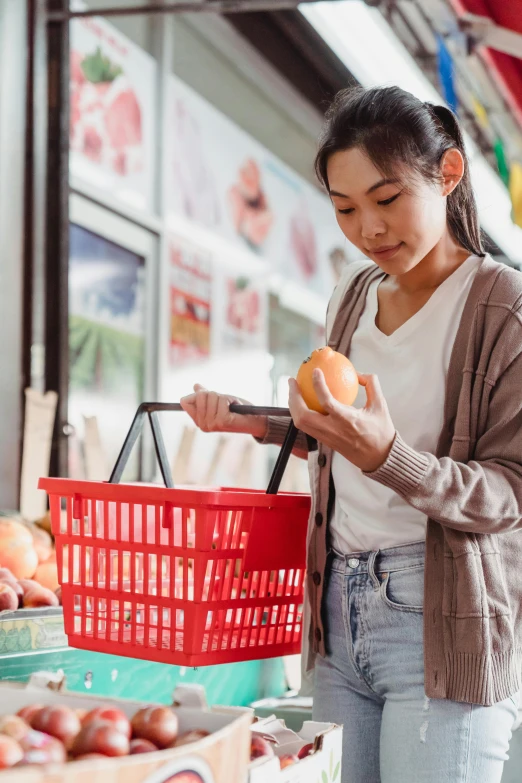 a woman is shopping in a grocery store, pexels, wearing an orange t-shirt, asian female, holding an apple, square