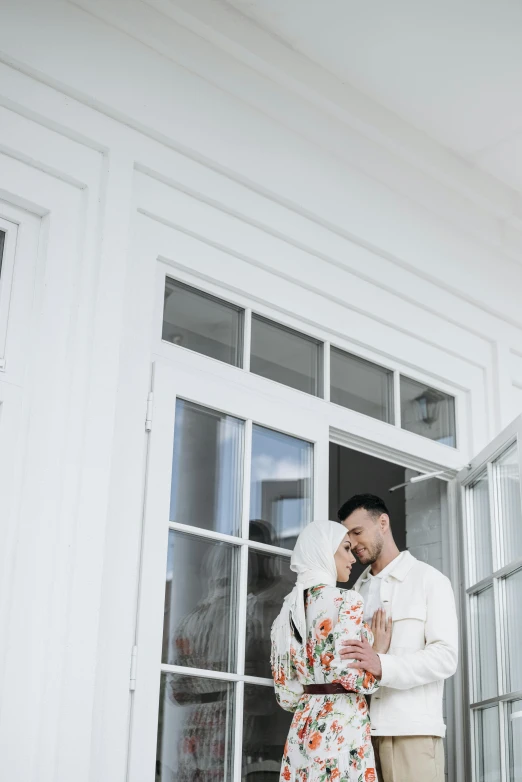 a man and a woman standing in front of a house, by Basuki Abdullah, pexels contest winner, romanticism, all white render, standing near a window, background image, islamic