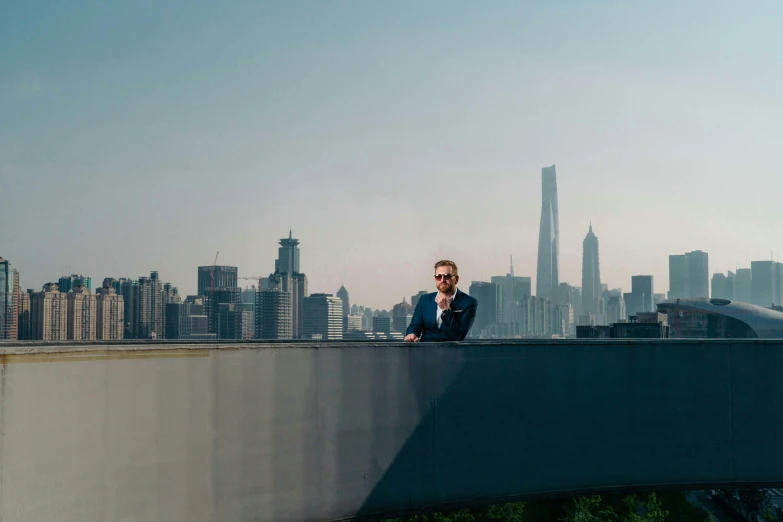 a man standing on a bridge with a city in the background, inspired by Zhang Kechun, pexels contest winner, happening, corporate boss, doing an elegant pose over you, matt rhodes, shanghai