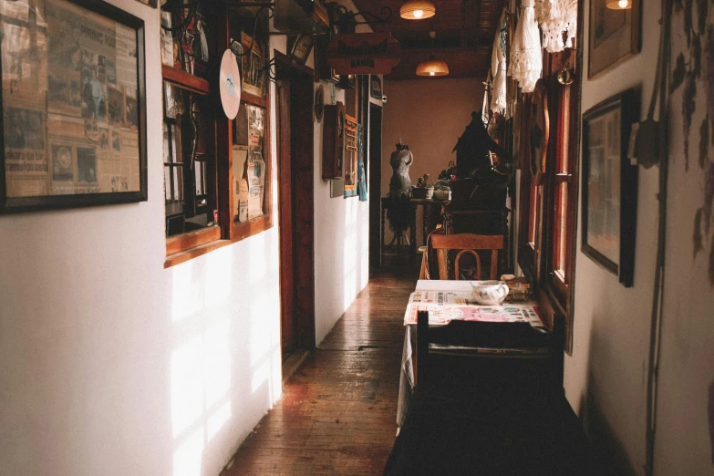 a hallway with a table and pictures on the wall, pexels contest winner, private press, old shops, sun flares, inside old cabin, crafts and souvenirs