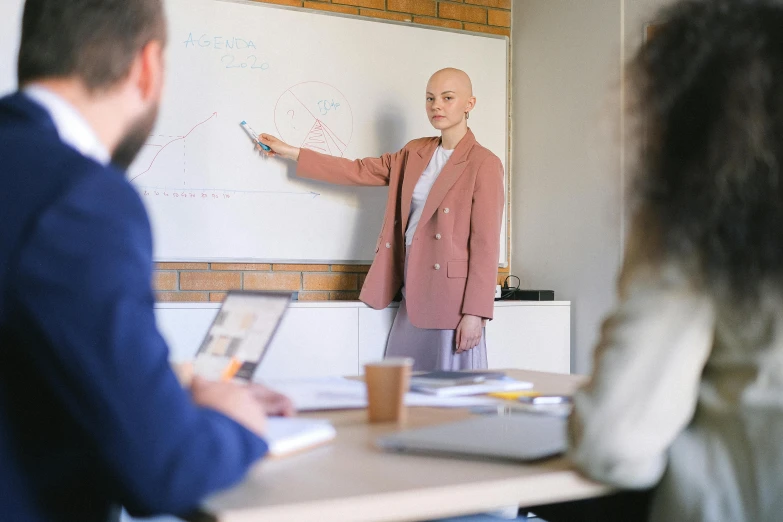 a man giving a presentation to a group of people, by Emma Andijewska, pexels, wearing a light - pink suit, bald, 30 years old woman, female in office dress