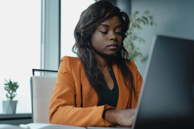 a woman sitting in front of a laptop computer, pexels, orange and black, african canadian, girl in a suit, concentration