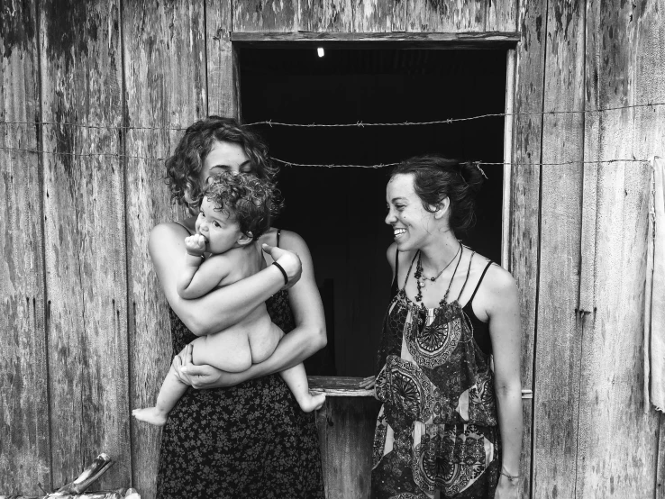 a black and white photo of two women holding a baby, by Caro Niederer, justina blakeney, leaning on door, happy people, in the countryside