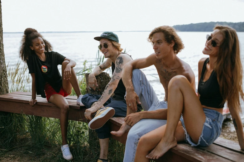 a group of young people sitting on top of a wooden bench, by Emma Andijewska, trending on pexels, with tattoos, shoreline, chilled out smirk on face, lookbook