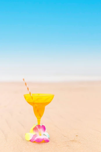 a yellow cocktail glass sitting on top of a sandy beach, profile image