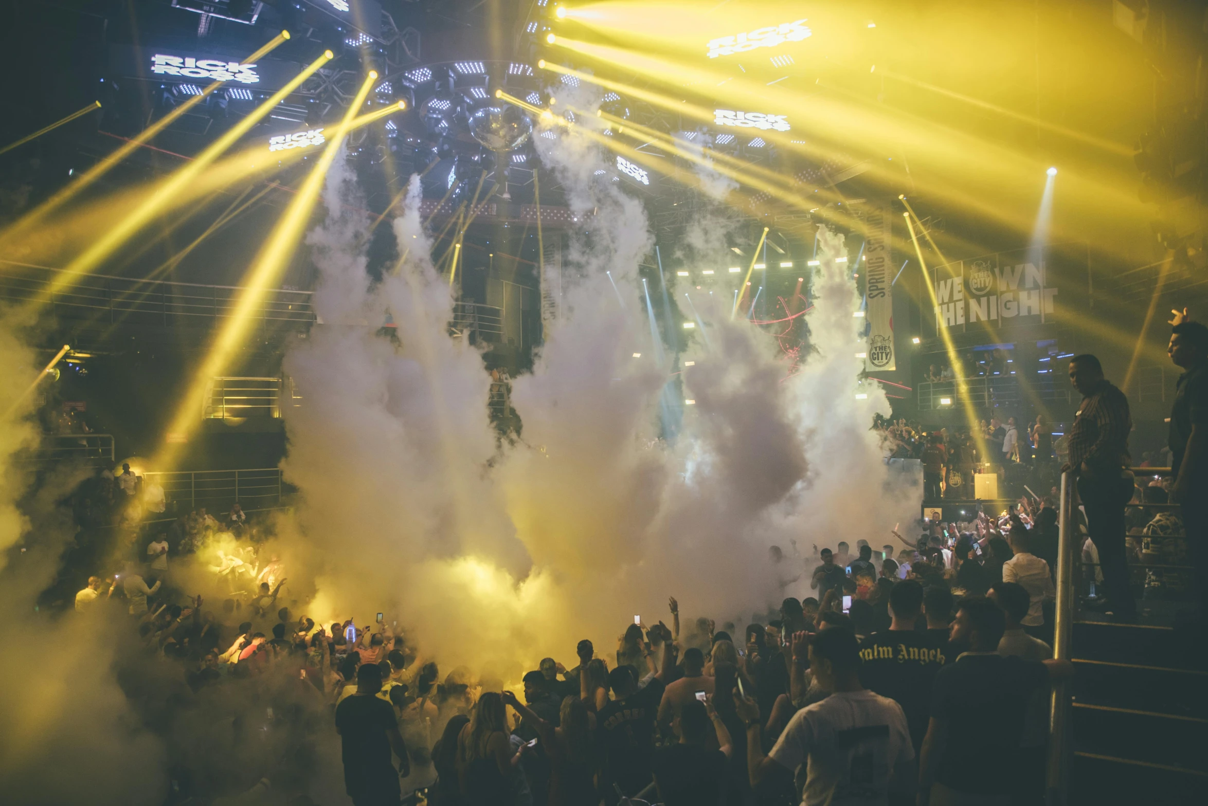 a crowd of people standing on top of a stage, by Niko Henrichon, happening, ibiza nightclub dancing inspired, dust mist, blue and yellow lighting, conor walton