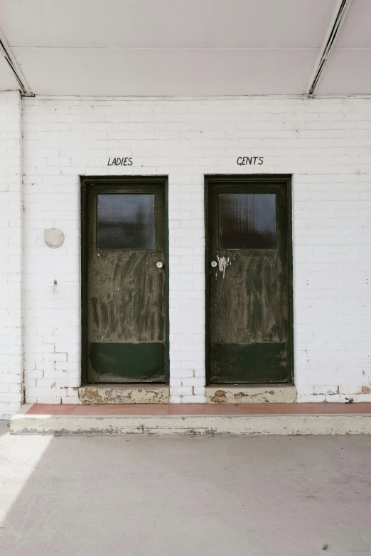 a white brick building with two green doors, an album cover, inspired by Tom Roberts, unsplash, visual art, toilet, lakes, ignant, vendors