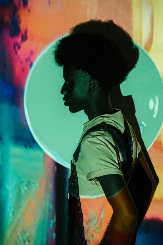 a man standing in front of a colorful wall, inspired by Gordon Parks, afrofuturism, lighting her with a rim light, jaylen brown, glowing sphere, woman's profile