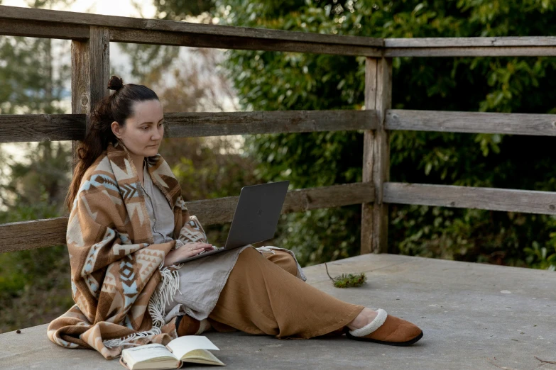 a woman sitting on a bench using a laptop computer, a portrait, inspired by Camille Corot, unsplash, art & language, brown cloak, full body in shot, still from the movie, covered with blanket