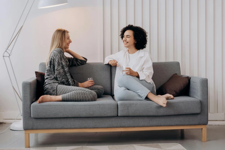 two women sitting on a couch talking to each other, pexels contest winner, minimalism, one blonde and one brunette, lounge room, grey, happy friend