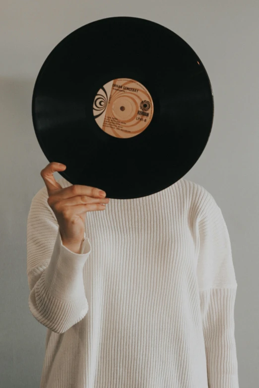 a woman holding a vinyl record in front of her face, trending on pexels, wearing a white sweater, background image, stems, full body image