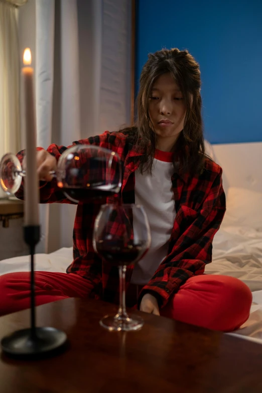 a woman sitting on a bed holding a glass of wine, lumberjack flannel, red and black colour scheme, pouring, uplit