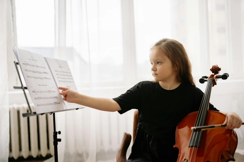 a little girl that is sitting down with a cello, by Elizabeth Durack, pexels contest winner, sheet music, looking partly to the left, panels, student