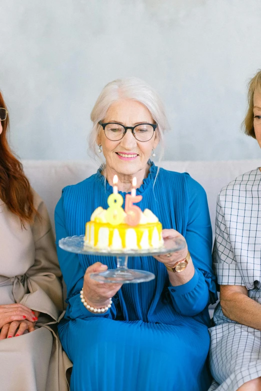three women sitting on a couch holding a cake, pexels contest winner, white haired lady, yellow, wrinkly, wearing small round glasses
