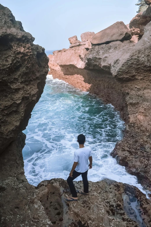 a man standing on top of a rock next to the ocean, dry archways, epic coves crashing waves plants, grotto, 2019 trending photo