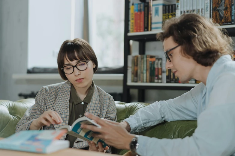 a man and a woman sitting on a couch looking at a book, pexels contest winner, girl wearing round glasses, avatar image, people at work, people sitting at tables