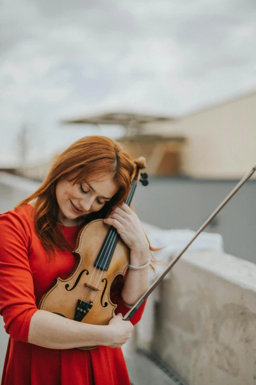 a woman in a red dress holding a violin, by Anna Haifisch, pexels contest winner, on rooftop, ( redhead, square, on a pale background