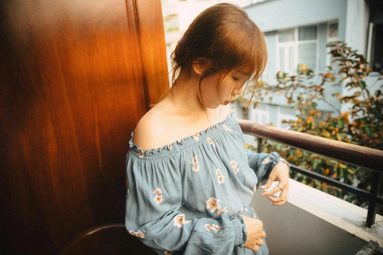 a woman standing on a balcony looking at her cell phone, inspired by Ni Yuanlu, tumblr, off the shoulder shirt, soft blue tones, floral embroidery, ulzzang
