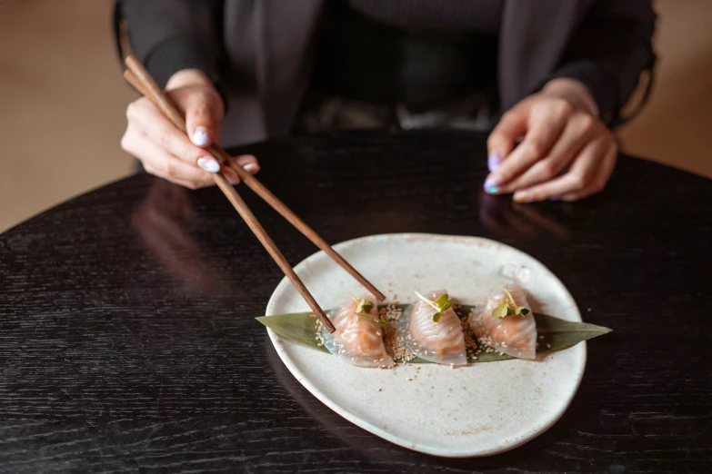 a close up of a plate of food with chopsticks, a portrait, by Julia Pishtar, trending on unsplash, two hands reaching for a fish, dumplings on a plate, sparkling, slightly tanned