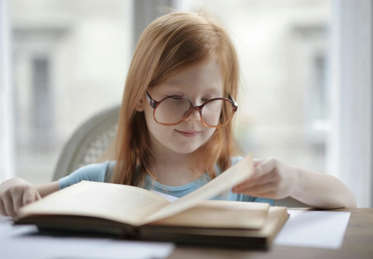 a little girl sitting at a table reading a book, pexels contest winner, square rimmed glasses, avatar image, college, restoration