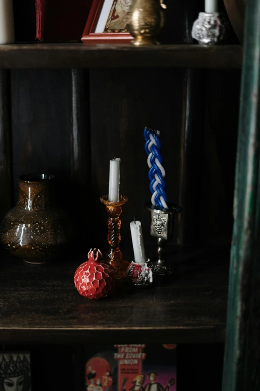 a book shelf filled with books and candles, a still life, unsplash, vanitas, glass beads clay amulets, prussian blue and venetian red, on a candle holder, detailed product shot