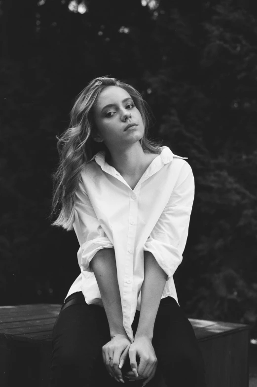 a black and white photo of a woman sitting on a bench, inspired by Emma Ríos, chloe grace moretz, wearing a white button up shirt, confident pose, square