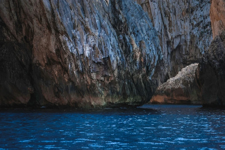 a large rock formation in the middle of a body of water, inspired by Fede Galizia, pexels contest winner, romanticism, dark blue water, panels, picton blue, natural cave wall