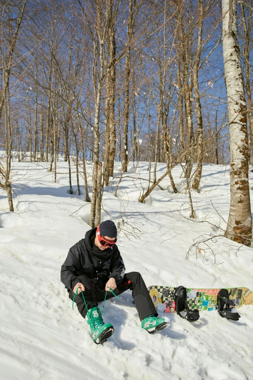 a man riding a snowboard down a snow covered slope, sitting under a tree, heavy birch forest, corduroy, snacks