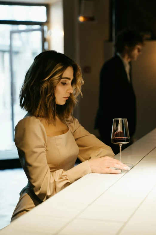 a woman sitting at a bar with a glass of wine, she's sad, slightly minimal, shy looking down, sad man