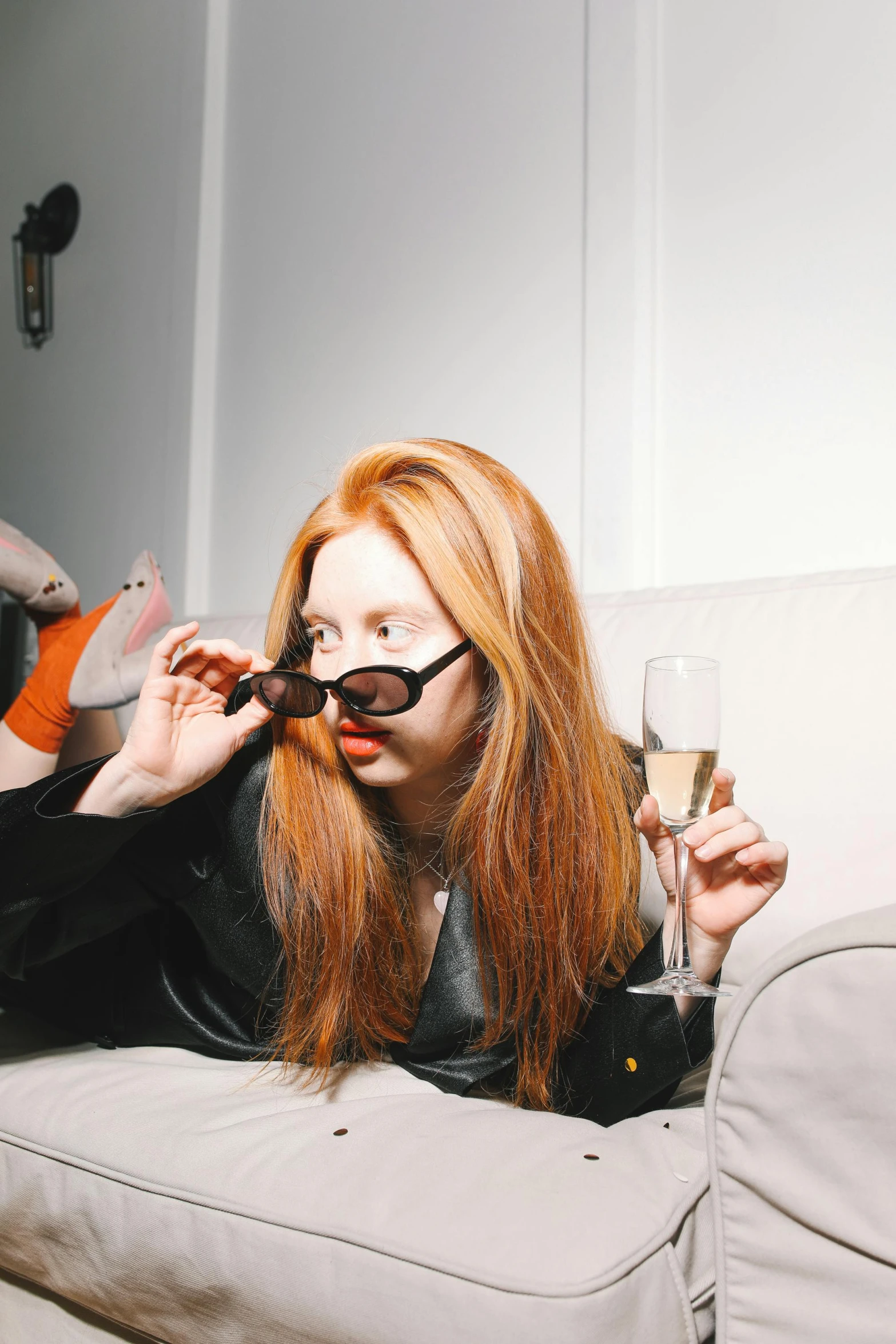 a woman laying on a couch with a glass of wine, inspired by Nan Goldin, trending on pexels, renaissance, long orange hair, wearing mirrored sunglasses, on a pale background, at the party
