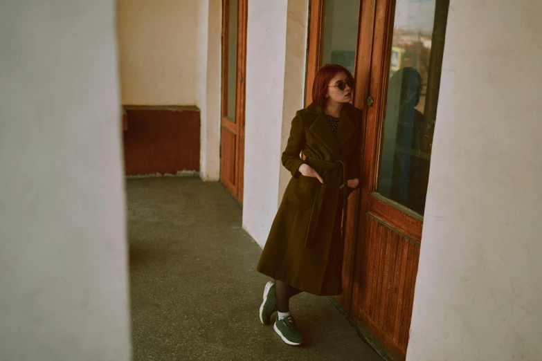 a woman in a green coat leaning against a wall, pexels contest winner, bauhaus, russian style, exiting store, brown tones, instagram picture