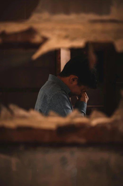 a man is looking through a hole in a wall, trending on unsplash, praying with tobacco, in a ravaged library, resting head on hands, asian male