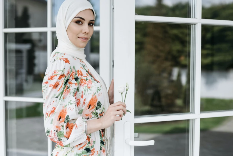 a woman wearing a hijab standing in front of a window, trending on pexels, hurufiyya, wearing floral chiton, white and orange, door, al fresco