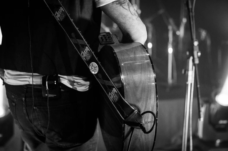 a man holding a guitar while standing in front of a microphone, by Neil Blevins, morning detail, uploaded, straps, back and white