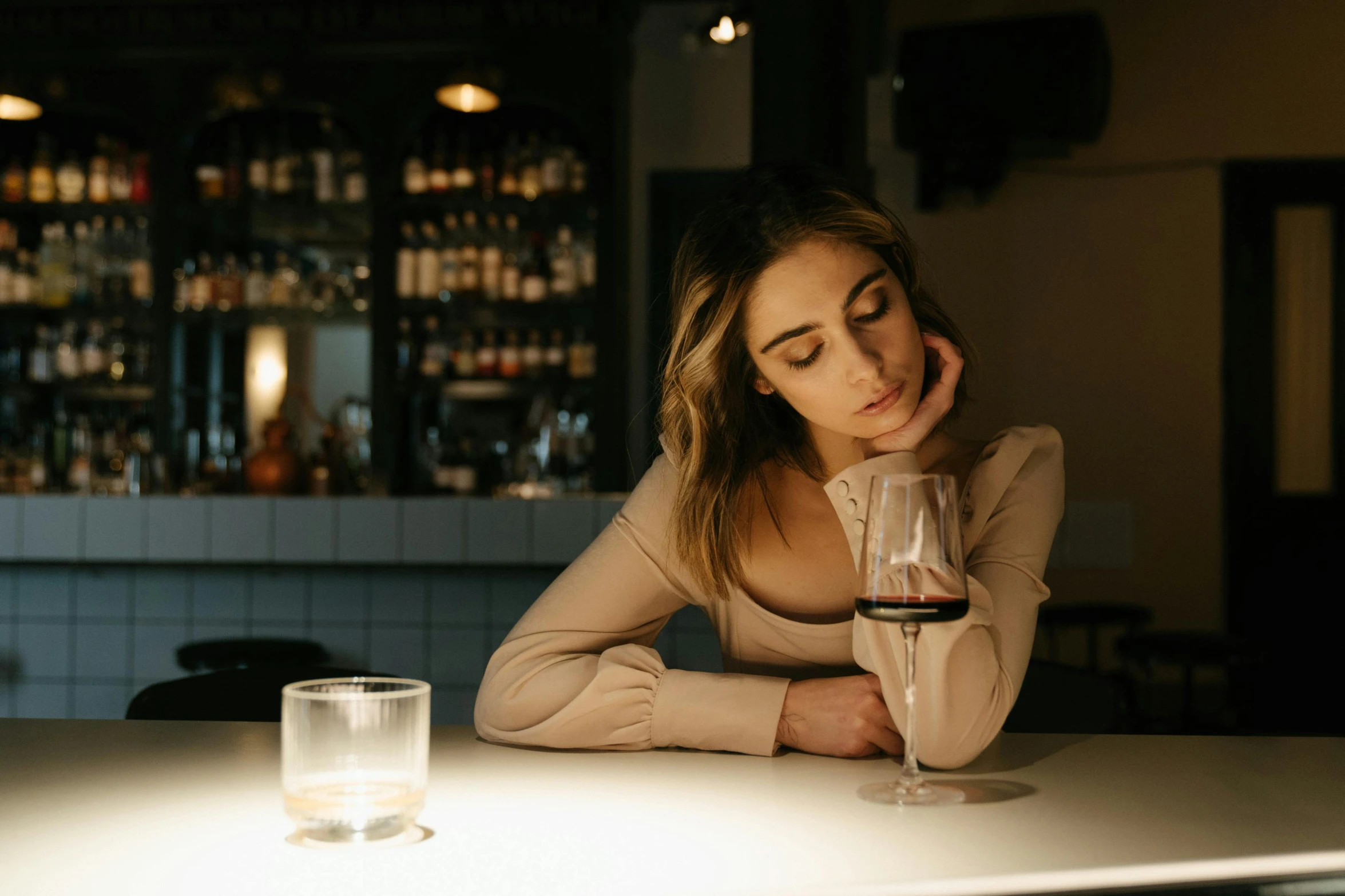 a woman sitting at a table with a glass of wine, a portrait, by Lee Loughridge, trending on pexels, sad lighting, sitting at the bar, sydney hanson, completely empty
