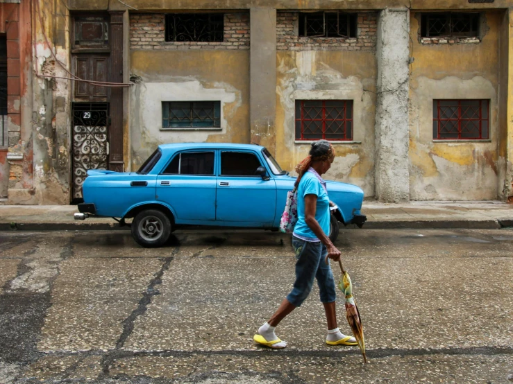 a woman walking across a street next to a blue car, by Emanuel Witz, pexels contest winner, cuban revolution, square, a wooden, aida muluneh