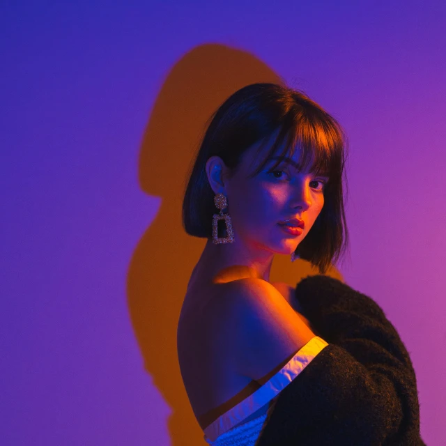 a woman standing in front of a purple wall, an album cover, inspired by Elsa Bleda, trending on pexels, realism, isabela moner, dramatic neon lighting, maisie williams, elegant profile pose