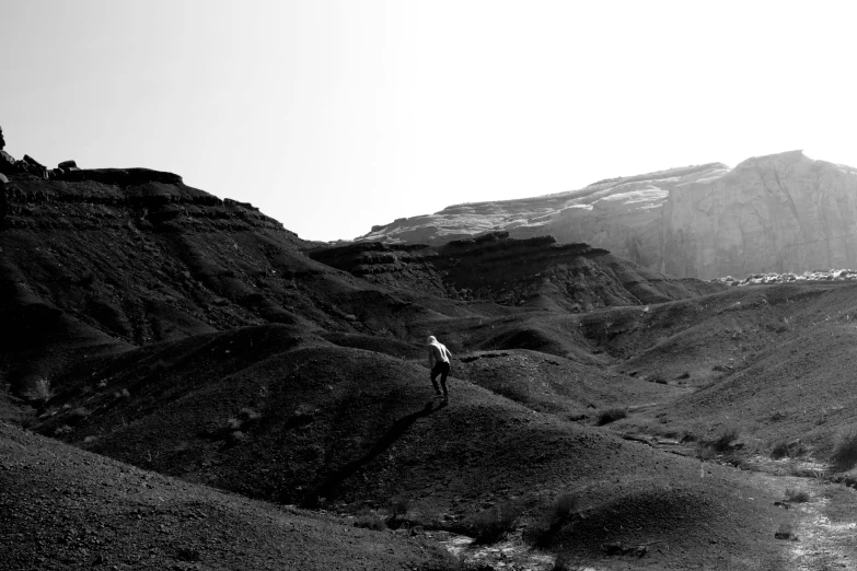a black and white photo of a person on a mountain, a black and white photo, by Ismail Acar, ambeint, the middle of a valley, humans exploring, charred desert