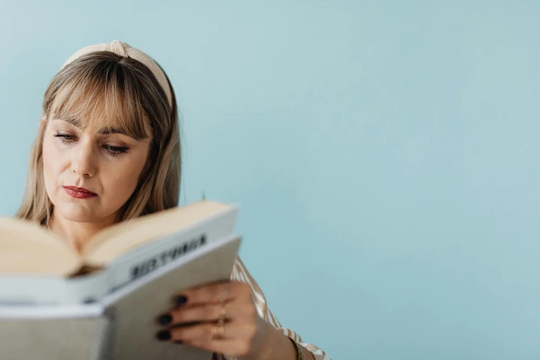 a woman reading a book while wearing a headband, a portrait, trending on pexels, figuration libre, with a blue background, over the shoulder, bedhead, student