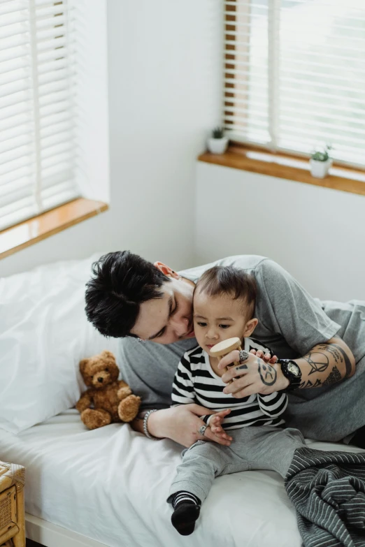 a man sitting on top of a bed holding a baby, pexels contest winner, morning coffee, emo, hugging each other, 1 4 9 3