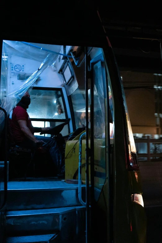 a man sitting in a bus looking out the window, during the night, with people inside piloting it, square, worksafe. cinematic