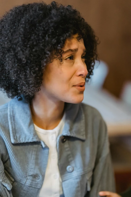a woman sitting at a table with a cell phone in her hand, a portrait, trending on pexels, renaissance, short black curly hair, compassionate, mixed race, profile image