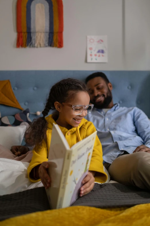 a man and a little girl sitting on a bed reading a book, a picture, by Washington Allston, pexels contest winner, girl wearing round glasses, on a yellow canva, diverse, tv still