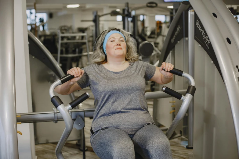 a woman sitting on a machine in a gym, pexels contest winner, an overweight, thumbnail, full faced, grey