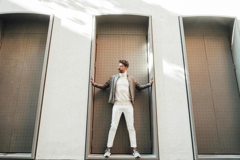 a man standing in the doorway of a building, inspired by david rubín, pexels contest winner, bauhaus, white trendy clothes, tan suit, attractive pose, metal framed portal