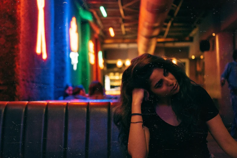 a woman sitting in a booth at a restaurant, inspired by Elsa Bleda, pexels contest winner, in a nightclub, she's sad, girl with dark brown hair, red and blue neon