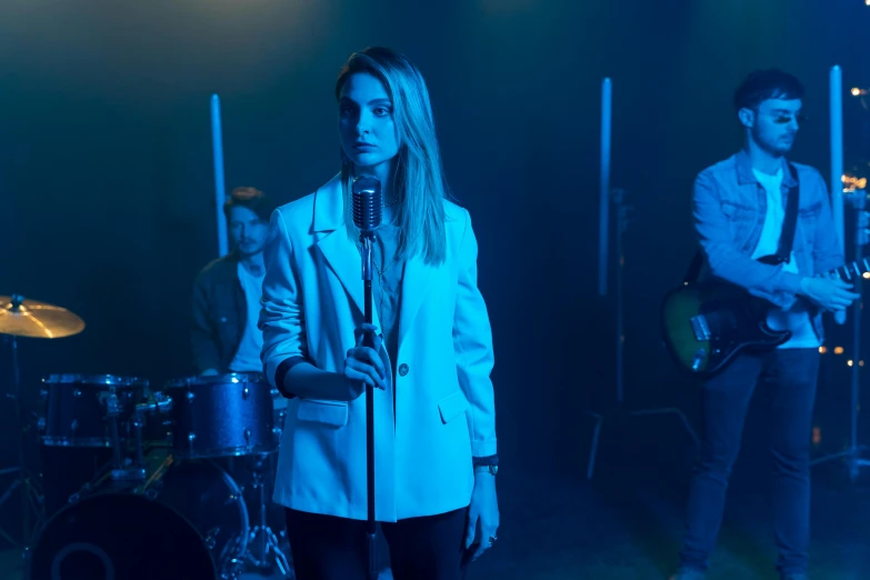 a woman standing next to a man on a stage, an album cover, pexels, antipodeans, ana de armas, blue jacket, movie still frame, musicians