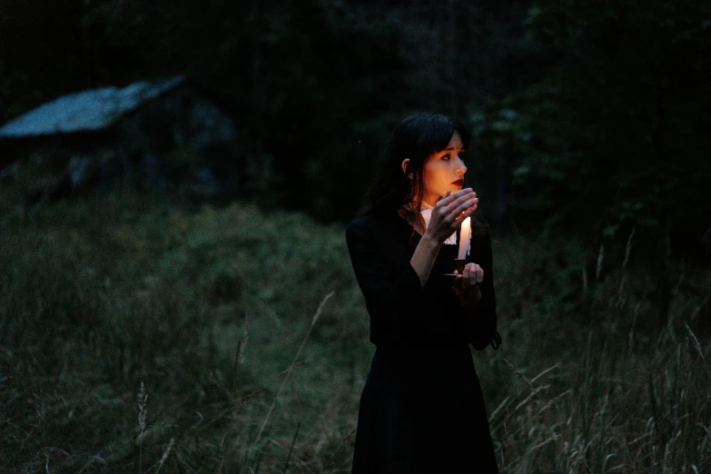 a woman standing in a field holding a lit candle, pexels contest winner, wearing a dark dress, profile image, forest ritual, concert