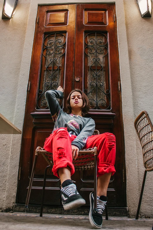 a woman sitting on a chair in front of a door, trending on pexels, graffiti, red sweater and gray pants, young spanish man, high soles, federation clothing